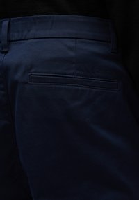 Granatowe spodnie o gładkiej fakturze, z jedną tylną kieszenią z haftowanym konturem oraz tłoczonym logo "Calvin Klein".