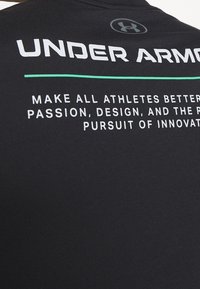 Svart atletisk tröja med vit text som visar märke och motiverande fraser. Materialet verkar slätt, med en figurnära design och rund hals.