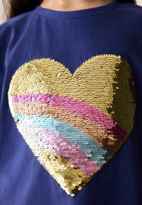 Camiseta navy con un gran corazón hecho de lentejuelas de colores en dorado, rosa, azul y marrón, con una superficie texturizada y brillante.
