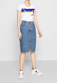 Džínová tužková sukně s předním rozparkem, světle modrá wash a designem s pěti kapsami. Vzhledem k bíl�é tričku s krátkým rukávem a bílým teniskám.