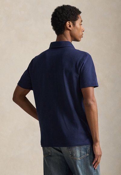 Μπλε ναυτικό πόλο πουκάμισο με τυπικό γιακά, κοντά μανίκια και υφασμάτινη υφή, συνδυασμένο με ανοιχτό μπλε τζιν. Απλός και κλασικός σχεδιασμός.