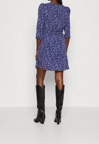 Sininen leopardinprinttinen mekko, jossa on kolmanneksen pituiset hihat, joustava vyötärö ja levenevä hame. Yhdistetty polviin ulottuviin mustiin saappaisiin.