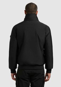 Svart polstret jakke med høy krage, elastiske mansjetter og ribbet kant. Glatt stoff med minimal maskinvare og et strømlinjeformet design.