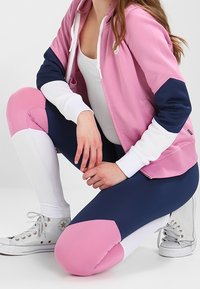 Felpa sportiva rosa e blu marina con accenti bianchi, abbinata a leggings blu marina e bianchi con toppe rosa sulle ginocchia e sezioni bianche sulle caviglie.