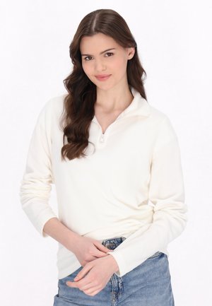Hvid fleece-pullover med halv-zip krave, lange ærmer og en blød tekstur, parret med blå denim jeans.