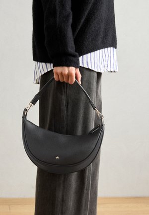 Bolso de mano de cuero negro con una silueta curva, superficie texturizada, asa corta y un sutil logo dorado en la parte frontal.