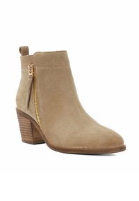 Bottine en suède beige avec un bout pointu, fermeture éclair dorée sur le côté et un talon en bois empilé, surface texturée.
