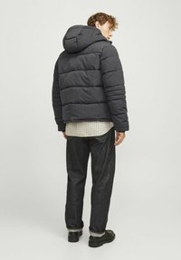 Sort dunjakke med hætte, der har vandret syninger og en tekstureret overflade, kombineret med mørk denim jeans og sorte sko.