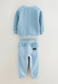 Lysblå børne-joggersæt bestående af en textured sweatshirt og matchende bukser, begge med ribbede detaljer og elastiske manchetter.
