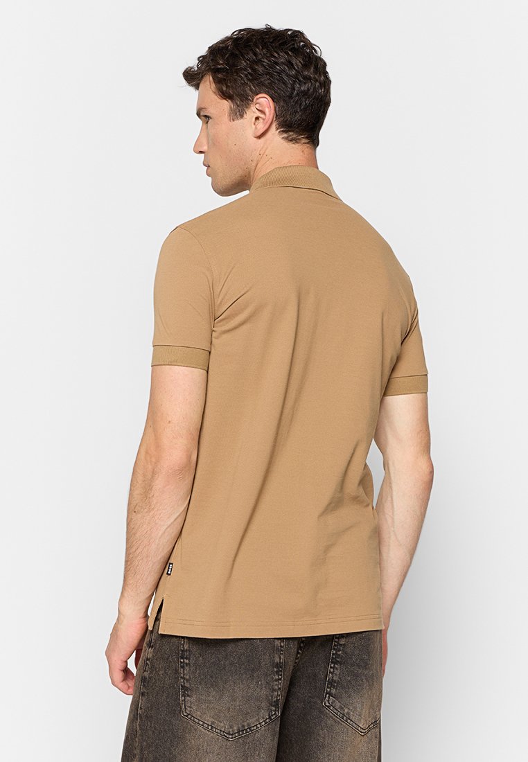 Polo shirt tan à manches courtes avec un col classique et des poignets côtelés, présentant un ourlet droit et des fentes latérales subtiles. Tissu doux et lisse.