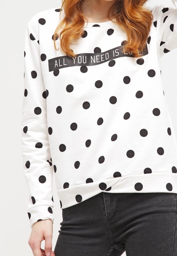 Biała bluza z czarnymi kropkami, ozdobiona poziomym czarnym paskiem z napisem „ALL YOU NEED IS LOVE”. Ściągacze na mankietach i u dołu bluzy.