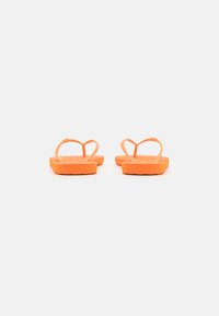 Tongs orange avec semelle texturée, fines lanières formant une boucle en haut, semelle plate et design minimaliste.