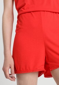 Czerwone bawełniane szorty z fakturowanym obszyciem ozdobionym pomponami. Model posiada elastyczny pas dla wygody.