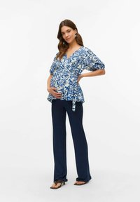 Graviditetsblus i blått blommönster, korta puffärmar, omlottdesign. Kombinerad med mörkblå ribbade byxor och svarta sandaler.