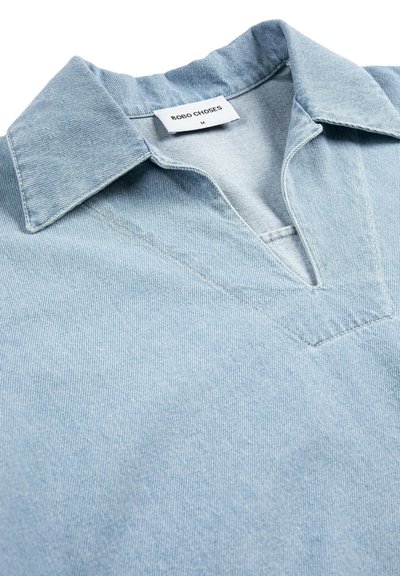 Chemise en denim bleu clair avec un col pointu, un décolleté en forme de V, et une étiquette "BOBO CHOSES" taille M à l'intérieur du col.