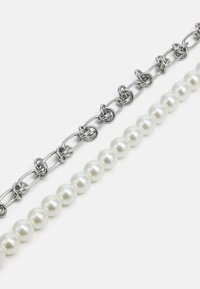 Collier en chaîne présentant des maillons en métal argenté entrecoupés de formes ovales, associé à une rangée de perles blanches rondes.