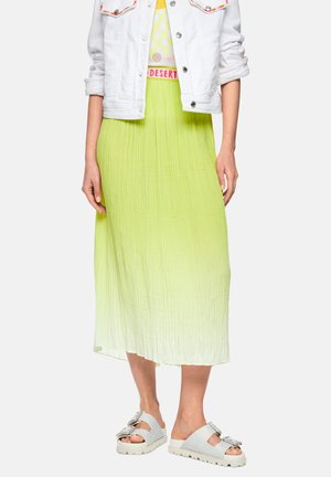 Woman wearing white cropped jacket, yellow-green ombre pleated midi skirt, and white open-toe sandals with buckles standing against plain background.