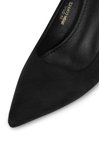 Pantofii cu toc înalt din suede negru au vârful ascuțit și o textură netedă. Interiorul are o căptușeală din piele; design minimalist fără accesorii suplimentare.