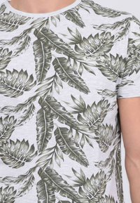 T-shirt à manches courtes gris clair avec un imprimé de feuilles vertes, doté d'un col rond et en coton doux et texturé.