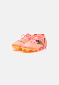Botas de fútbol con un degradado en rosa y naranja, que cuentan con una parte superior texturizada, acento de logo negro y múltiples tacos de goma en la suela.