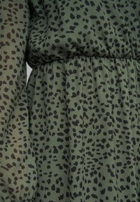 Roheline kangas mustade ebaühtlaste leopardilaadsete laikudega ja kogutud elastse vöökohaga detail.