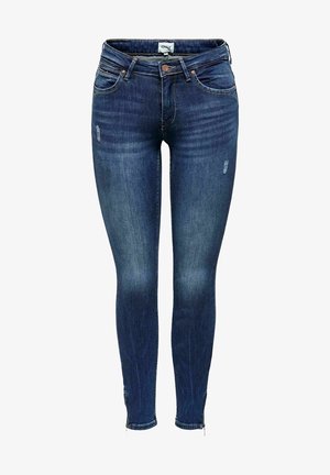 Jean skinny en denim bleu foncé, avec des détails usés et une taille standard. Le tissu a une texture lisse et épouse étroitement la silhouette.