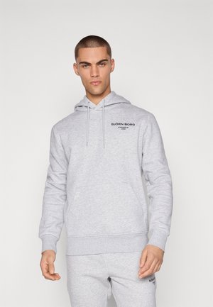 Male model wearing light gray Björn Borg hoodie and matching sweatpants, standing against a plain white background.