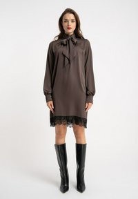Brązowa jedwabna sukienka z długimi rękawami, dekoltem z kokardą i czarną koronką na dole. Noszona z czarnymi kozakiem na obcasie do kolan.
