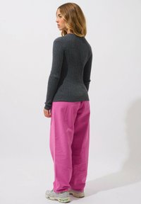 Maglione grigio a coste con maniche lunghe, abbinato a pantaloni larghi rosa acceso e sneakers grigie chiare. Design semplice e tessurizzato.