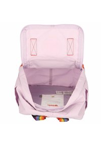 Interior de mochila lilás claro com textura suave, apresenta costura laranja, duas alças verticais e etiquetas visíveis na base.