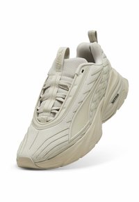 Jasnobeżowe buty sportowe z teksturowaną siateczką na górze, zaokrąglonym noskiem i amortyzowaną podeszwą. Charakteryzują się starannym przeszyciem i pętelką.