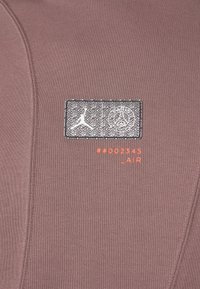 Sweat-shirt de sport marron avec un patch logo texturé présentant un design noir et blanc et un texte orange "#002345 _AIR."