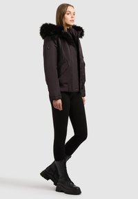 Schwarze Pufferjacke mit Kunstfellkapuze, ausgestattet mit Seitentaschen, gerippten Bündchen und einem lockeren Schnitt, kombiniert mit schwarzen Leggings und Kampfstiefeln.