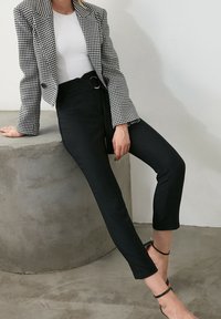 Svarta skräddarsydda byxor med hög midja och ankellängd, i kombination med en kavaj med houndstooth-mönster. Kavajen har en strukturerad passform och krage.