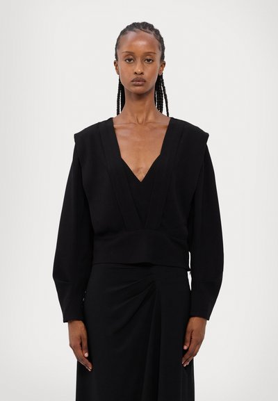 Black long-sleeve top with deep V-neck and structured shoulders, paired with a matching draped black skirt. Smooth texture, minimalistic design.