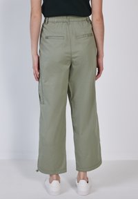 Kaki cargobyxor med elastisk midja, sidofickor och kort, bred ben-design. Slät textur och snörningsdetalj vid bensluten.