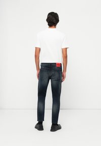 Jeans de denim azul oscuro con un corte slim, que presentan un parche de marca rojo en la parte trasera, y una camiseta blanca lisa. Textura suave, diseño minimalista.