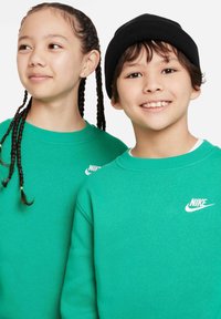 Dvoje djece nose usklađene svijetlozelene Nike dukserice. Dukserice imaju okrugli izrez i ističu bijeli Nike logo sprijeda. Jedno dijete nosi crnu kapicu.