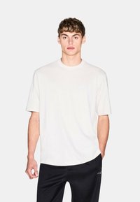 T-shirt bianco in cotone con scollatura rotonda, maniche corte e un logo del marchio discreto sul davanti. Abbinato a pantaloni sportivi neri.