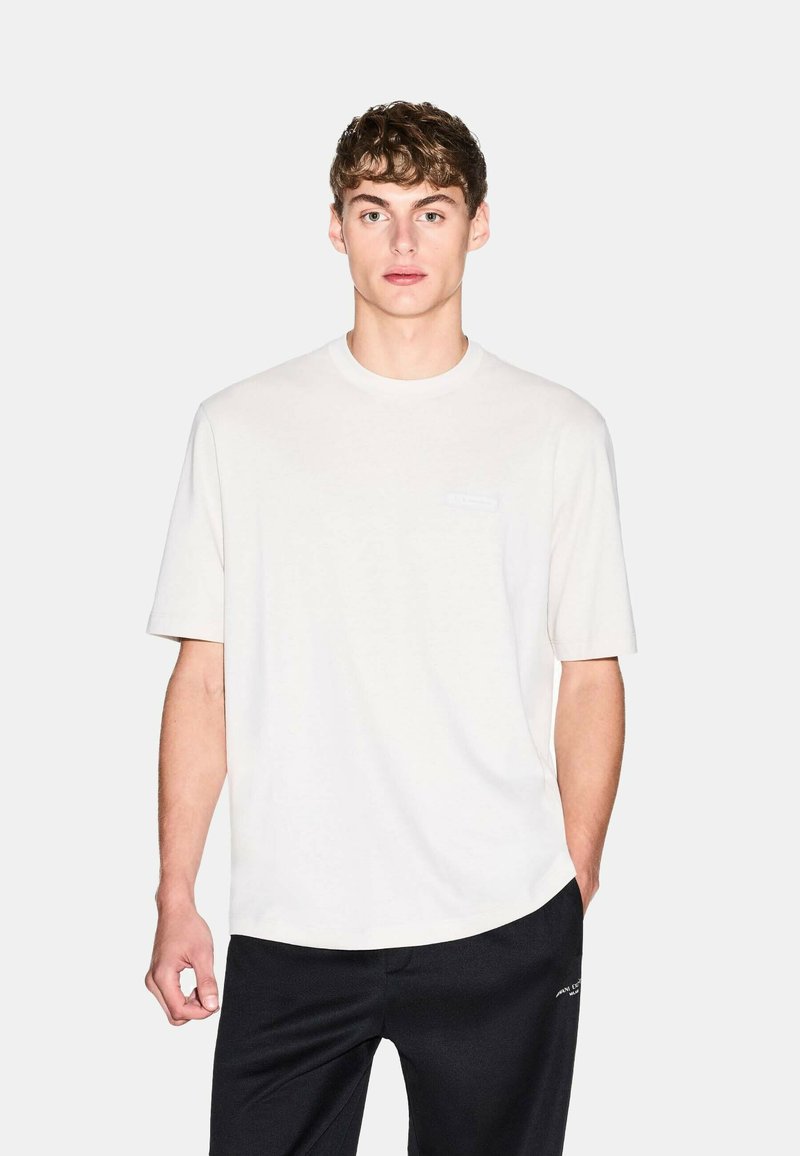 T-shirt bianco in cotone con scollatura rotonda, maniche corte e un logo del marchio discreto sul davanti. Abbinato a pantaloni sportivi neri.