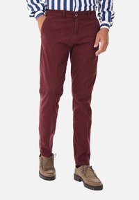 Chinos bordeaux in cotone con vestibilità slim, dotati di chiusura frontale con bottone, tasche laterali e indossati con scarpe in suede marrone chiaro.