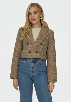 Veste brune courte à double boutonnage, en tissu texturé avec de grands boutons, associée à un jean taille haute bleu et un haut léger.