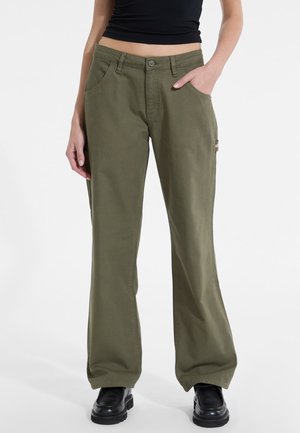 Pantaloni a gamba larga verde oliva realizzati in cotone robusto, dotati di tasche laterali e chiusura con bottone, abbinati a un top nero e scarpe chunky.