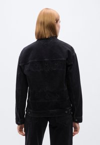 Μαύρο τζιν μπουφάν με κλασικό σχεδιασμό, άνετη εφαρμογή, λεπτομέρεια λογότυπου στην πλάτη και κουμπιά στα μανίκια για ρυθμιζόμενη εφαρμογή.