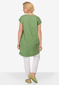 Zelený tunik s krátkým rukávem, rovného střihu a kulatým výstřihem. V kombinaci s bílými kalhotami a zelenými nazouvacími botami. Hladký povrch.