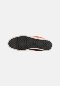 Fekete gumitalppal rendelkező sneaker, amelyen tapadásmintázat található. Világos bézs színű középtalpa és narancssárga felső része van. Simára csiszolt textúra, az talpon logóval.