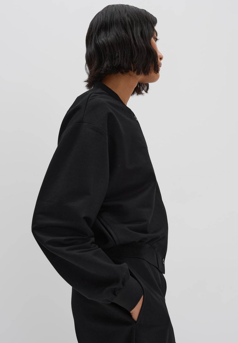 Schwarzer Sweatshirt mit Rundhalsausschnitt, langen Ärmeln, elastischen Bündchen und lockerer Passform. Glatte Textur und minimale Details.