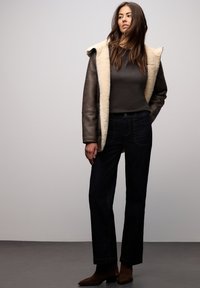 Brązowa skórzana kurtka z kremowym kołnierzem z futerka, szary top i ciemnoniebieskie dżinsy. Dopełnieniem stroju są brązowe botki za kostkę.