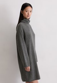 Szary sweter dress z wysokim kołnierzem, luźnym fasonem, długimi rękawami i ściągaczami, wykonany z miękkiego, teksturowanego materiału.