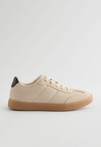 Beige sneakers med en struktureret canvas-overdel, snørebånds Lukning og gummisål. Har en sort detalje ved hælen og tre perforeringsdetaljer.